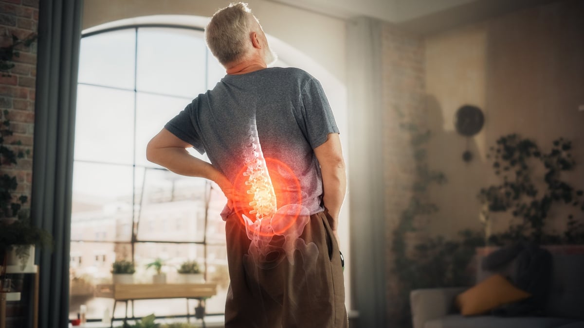 Senior male experiencing back pain from spine trauma or arthritis, massaging and stretching to ease the injury.