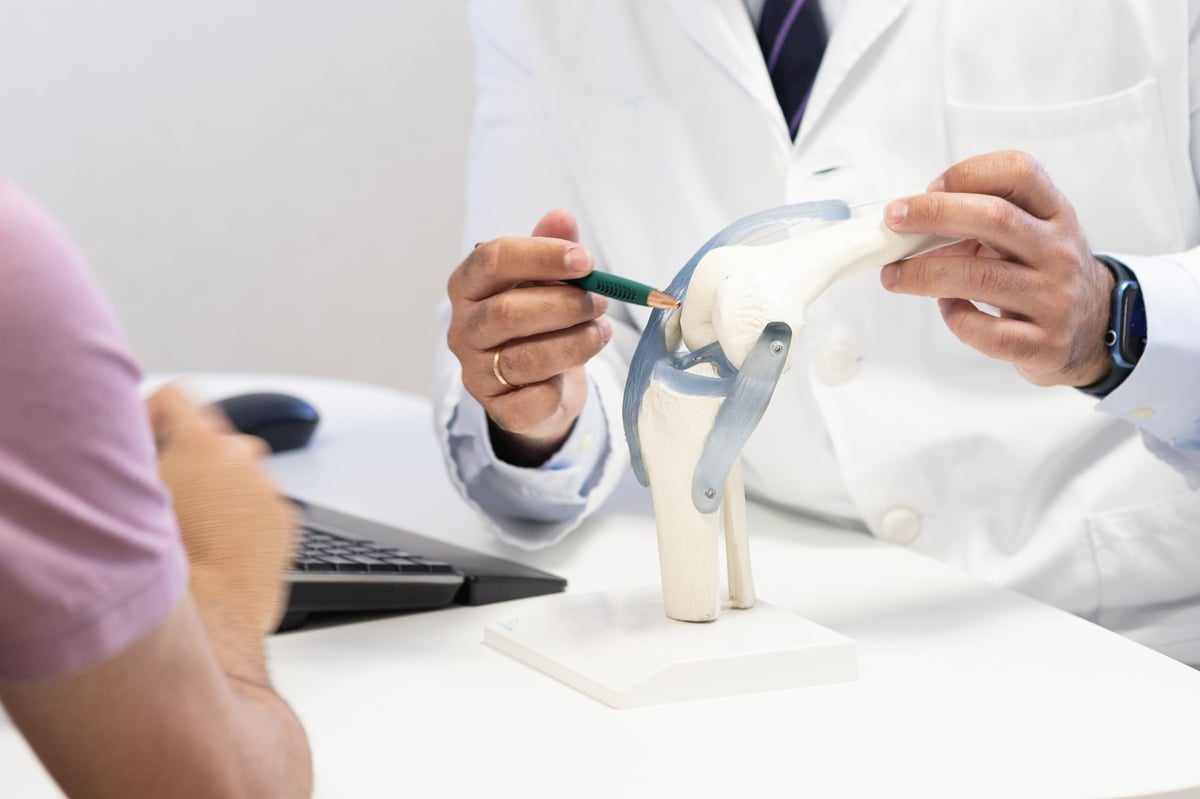 Doctor pointing at a detailed knee model to explain ligament functions to a patient, emphasizing joint health and treatment options