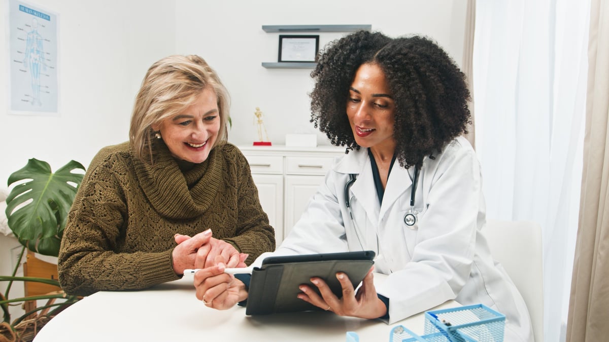 A warm medical scene where a doctor explains information on a tablet to an older patient in a bright clinic. Professional care, trust, and clear communication.