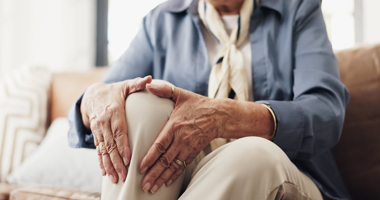 Hands, knee pain and injury in sofa in home with fatigue, arthritis and muscle sprain in retirement. Elderly person, joint ache and fibromyalgia with inflammation on couch in living room at house